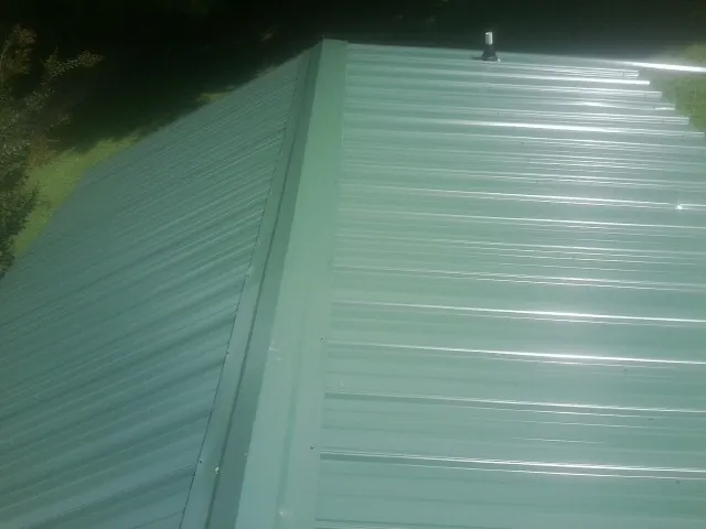 New green metal panels meeting at the ridge of a roof — Flat Roof Repair work by our crew in Rushville