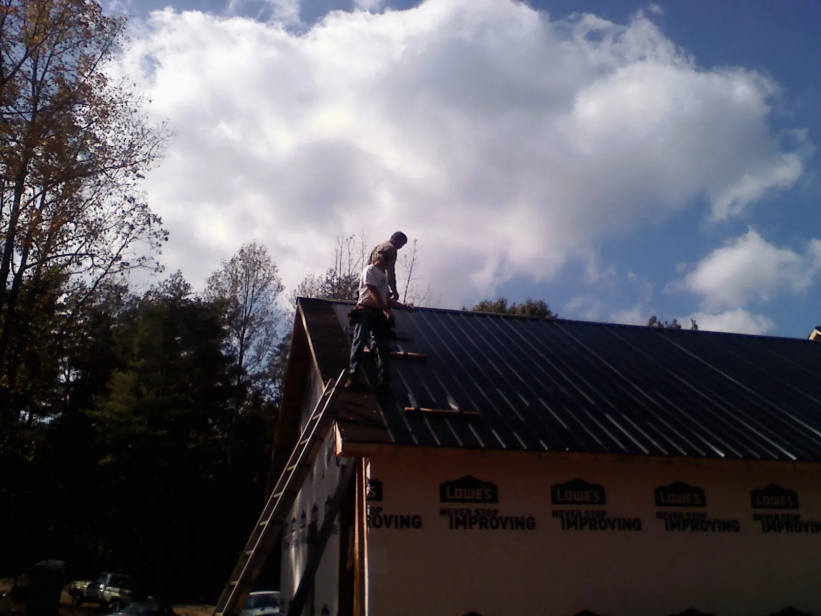 Roofer fastening dark metal panels high against a cloudy sky, from a Roof Inspection job in Rushville