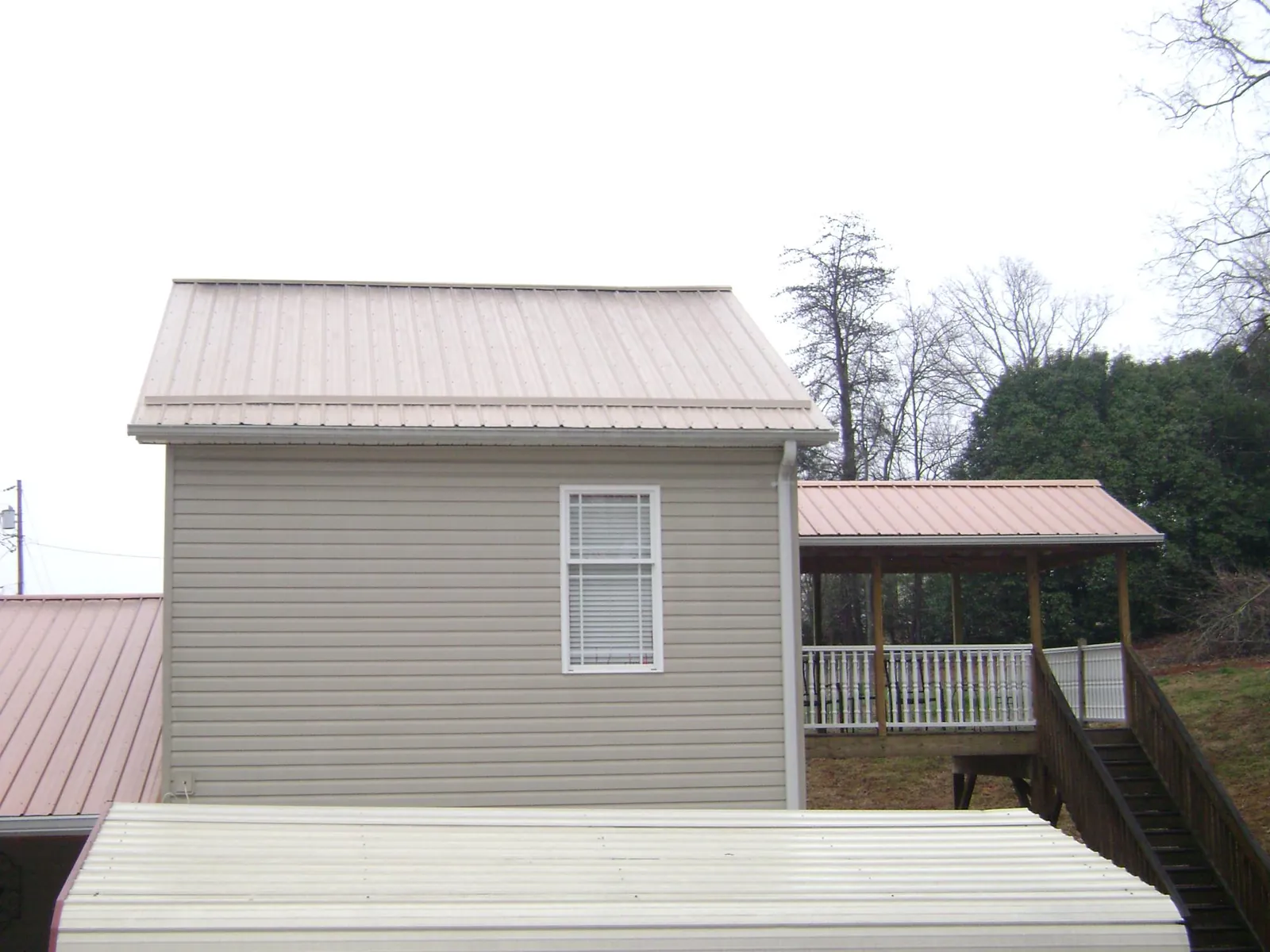 Tan metal roofs on a two story addition and attached porch, from a Roof Replacement job in Rushville